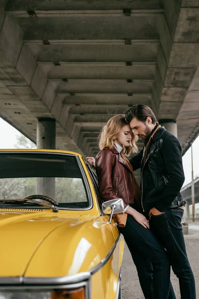 Vue latérale de élégant jeune couple étreignant près jaune ancienne voiture — Photo de stock