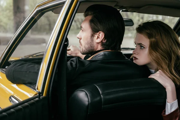Вид сзади красивой стильной молодой пары, сидящей вместе в ретро-машине — стоковое фото