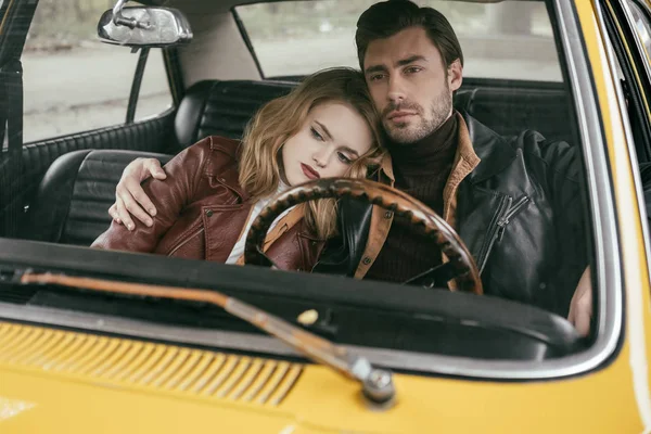 Elegante pareja joven reflexivo en chaquetas de cuero sentados juntos en coche pasado de moda — Stock Photo