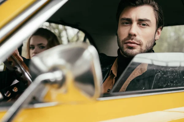 Handsome young man looking at camera while sitting with girlfriend in old-fashioned automobile — Stock Photo