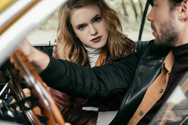 Beautiful young woman looking at camera while handsome boyfriend driving car — Stock Photo