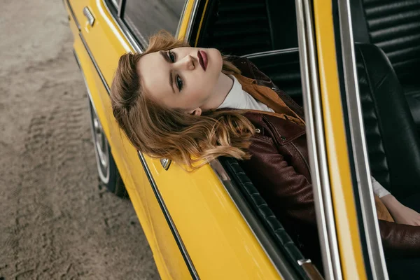 Високий кут зору стомлююча чуттєва дівчина сидить в жовтому класичному автомобілі — стокове фото