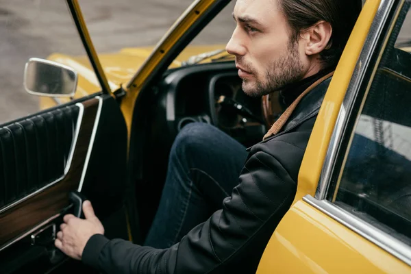 Seitenansicht des hübschen, stilvollen Mannes, der die Tür öffnet und wegschaut, während er im Retro-Auto sitzt — Stockfoto