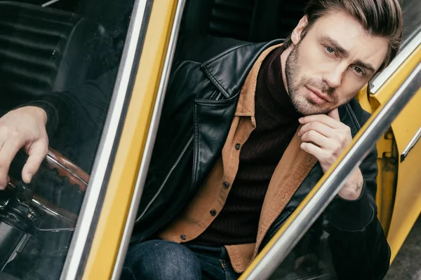 Pensive handsome young man sitting in classic car and looking at camera — Stock Photo