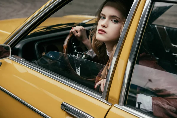 Attractive young woman looking at camera while sitting in yellow car — Stock Photo