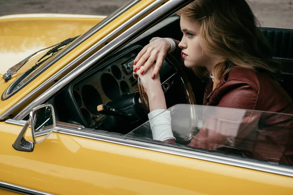 Menina bonita inclinando-se no volante e olhando para longe, enquanto sentado em carro amarelo — Fotografia de Stock