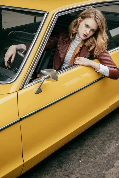 Beautiful stylish girl looking at camera through window of yellow retro car — Stock Photo