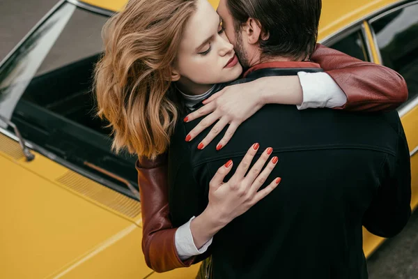 Высокий угол зрения на стильную молодую пару, обнимающую возле желтого автомобиля — Stock Photo