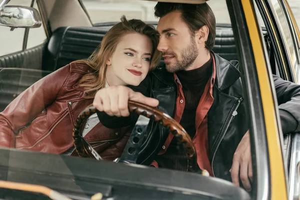 Hermosa joven pareja sonriente en chaquetas de cuero sentados juntos en el coche clásico - foto de stock