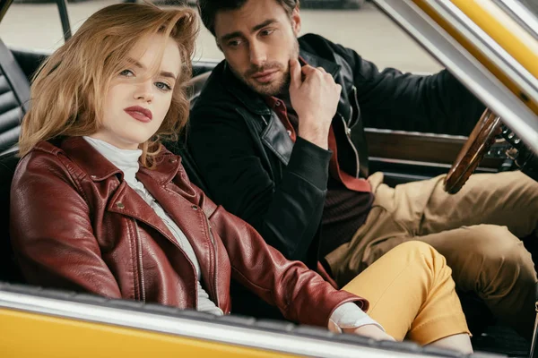 Elegante jovem casal em jaquetas de couro sentados juntos no carro vintage — Fotografia de Stock