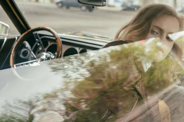 Vue à travers la fenêtre de belle fille assise dans une voiture vintage — Photo de stock