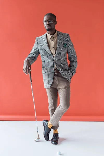 Golfista afroamericano alla moda con mazza da golf e palla, su rosso — Foto stock