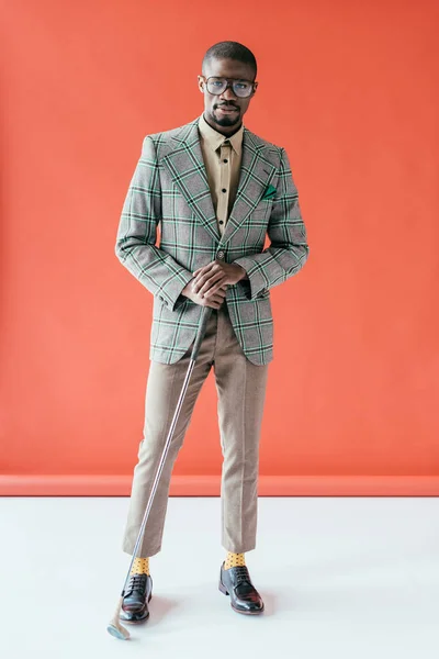 Young stylish african american golfer with golf club, on red — Stock Photo