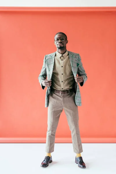 Homme afro-américain à la mode en lunettes et veste rétro posant sur rouge — Photo de stock