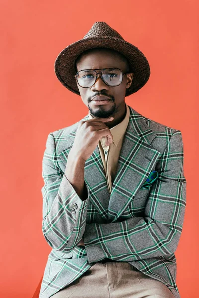 African american man in trendy eyeglasses and hat posing for vintage fashion shoot, isolated on red — Stock Photo