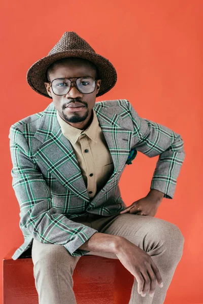 Hombre afroamericano de moda posando en gafas y sombrero vintage, aislado en rojo - foto de stock