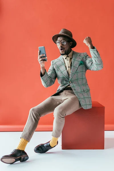 Успішний афроамериканський чоловік у старовинній куртці за допомогою смартфона, на червоному — стокове фото