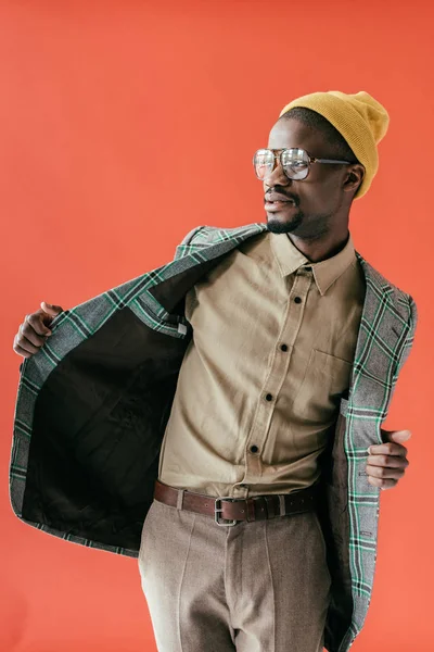 Hombre afroamericano de moda posando en gafas vintage y chaqueta, aislado en rojo - foto de stock
