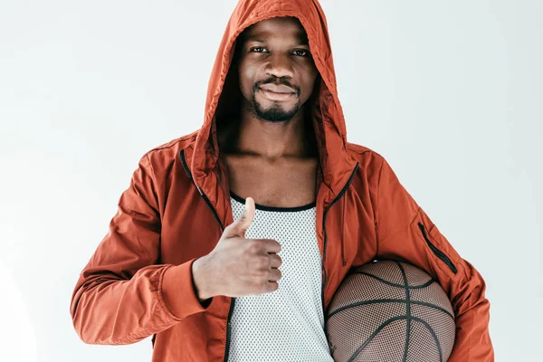 Hombre afroamericano con el pulgar hacia arriba sosteniendo la pelota de baloncesto, aislado en blanco - foto de stock