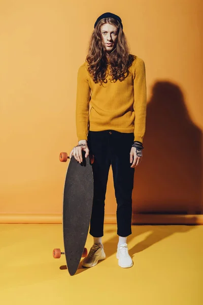 Junge stylische Skaterin stehend mit Longboard, auf gelb — Stockfoto