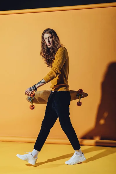 Stylish tattooed skateboarder with longboard, on yellow — Stock Photo
