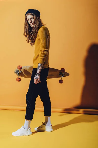 Stylish handsome skater holding longboard, on yellow — Stock Photo