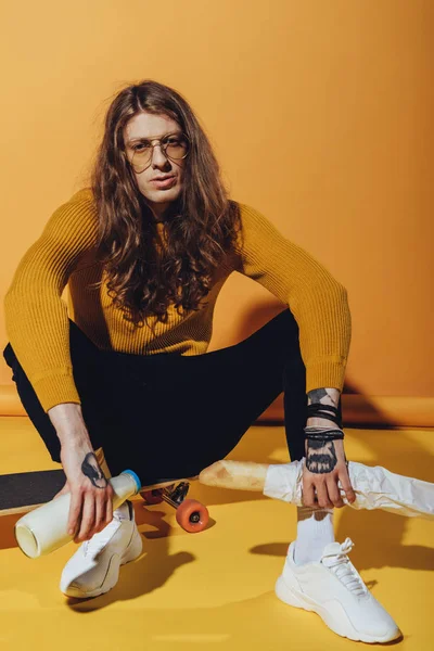 Hombre elegante sentado en longboard con leche y baguette, en amarillo - foto de stock