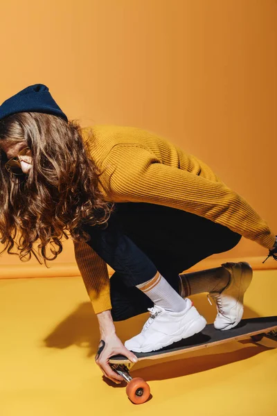 Stylish man with long hair sitting on longboard, on yellow — Stock Photo