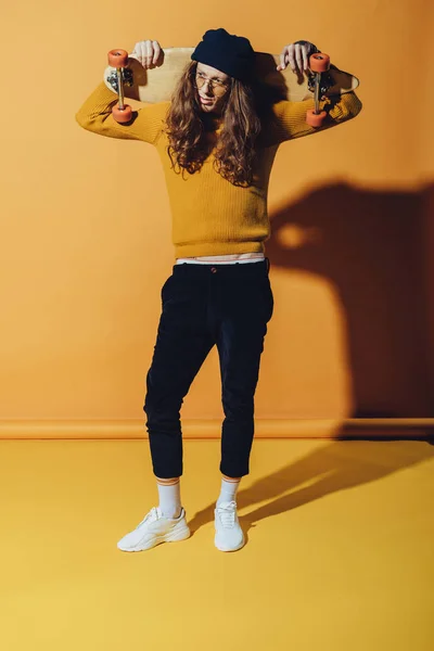 Young fashionable man posing with longboard, on yellow — Stock Photo