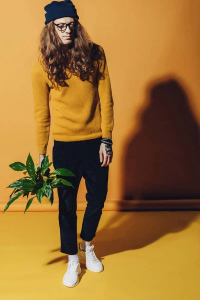 Fashionable man posing with plant, on yellow — Stock Photo