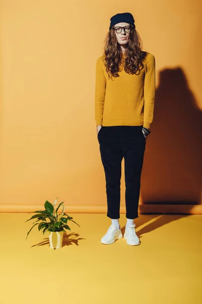 Модний чоловік з довгим волоссям, що стоїть біля рослини, на жовтому — стокове фото