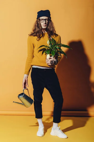 Fashionable male model posing with watering can and plant, on yellow — Stock Photo