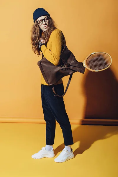 Handsome man with vintage backpack and wooden tennis racket, on yellow — Stock Photo