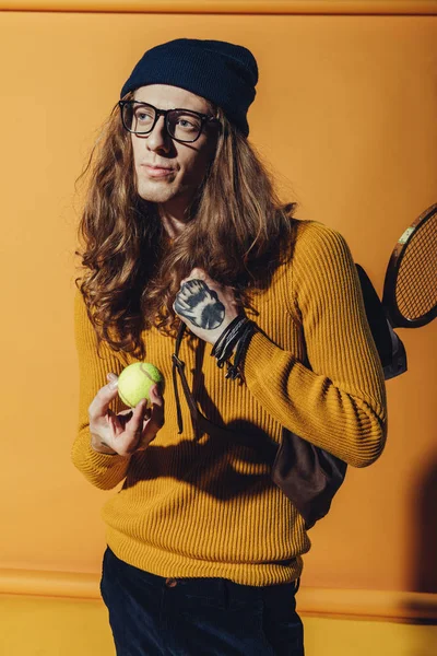 Stylish man with long hair holding tennis ball, on yellow — Stock Photo