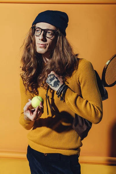 Stilvoller Mann mit langen Haaren hält Tennisball, auf gelb — Stockfoto