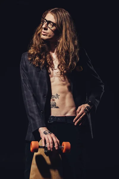 Fashionable tattooed skateboarder posing isolated on black — Stock Photo