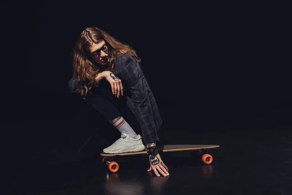 Stylish man with long hair posing with longboard, on black — Stock Photo