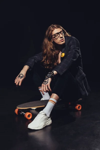 Fashionable man posing with longboard, on black — Stock Photo