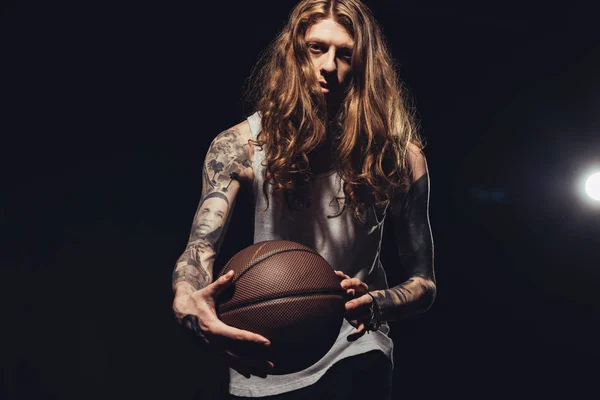 Stylische tätowierte Mann mit Basketballball, isoliert auf schwarz mit Hintergrundbeleuchtung — Stockfoto