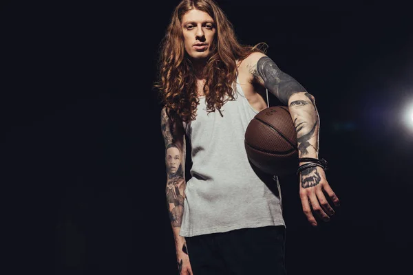 Hombre tatuado posando con pelota de baloncesto, aislado en negro con luz de fondo - foto de stock