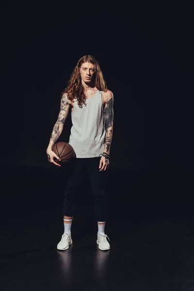 Tattooed man standing with basketball ball, on black — Stock Photo