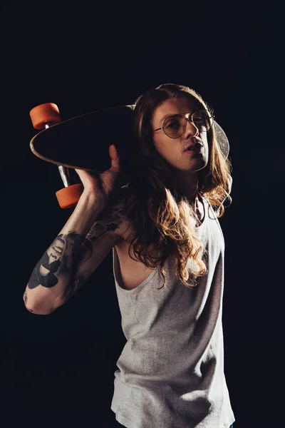 Homem elegante posando com skate, isolado em preto — Fotografia de Stock