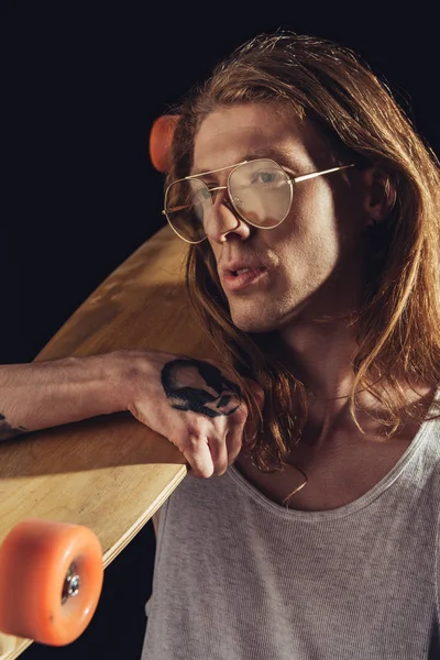 Stylish man with long hair holding longboard, isolated on black — Stock Photo