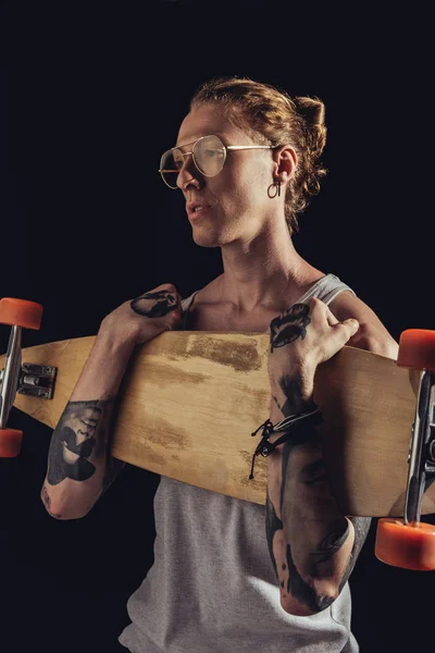 Fashionable tattooed man holding longboard, isolated on black — Stock Photo