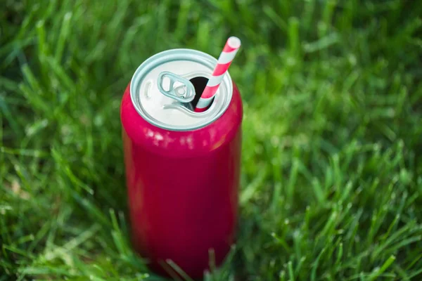 Close up view of drink in pink can with straw on green lawn — Stock Photo