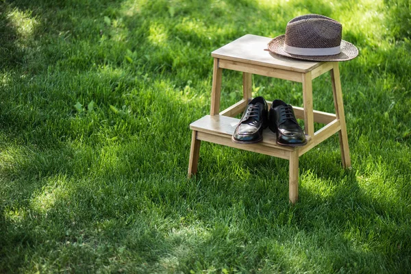 Vista ravvicinata di scarpe in pelle nera e cappello di paglia disposti su scale in legno su prati — Foto stock