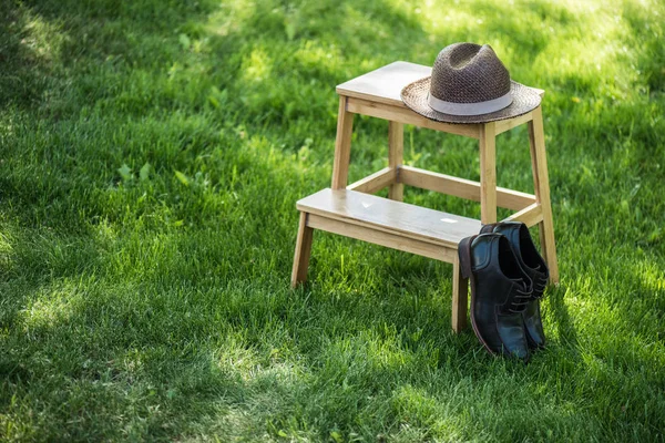 Close up view of arranged black leather shoes and straw hat on wooden stairs on grassland — Stock Photo