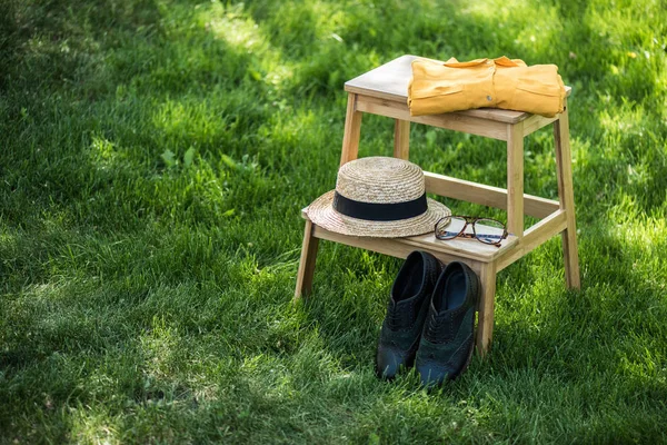 Nahaufnahme der Anordnung von Brille, schwarzen Schuhen, Hemd und Hut auf Holztreppen auf grünem Gras — Stockfoto