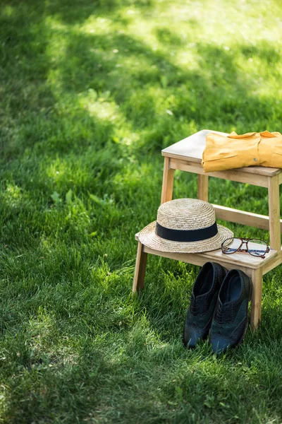 Close up view of arrangement of eyeglasses, black shoes, shirt and hat on wooden stairs on green grass — Stock Photo