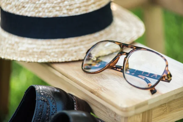 Close up view of arrangement of eyeglasses, black shoes and hat on wooden stairs on green grass — Stock Photo